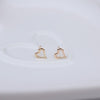 A pair of small gold heart-shaped stud earrings resting on a white ceramic dish.