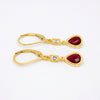 A pair of gold leverback earrings featuring teardrop-shaped deep red gemstones and small clear rectangular accent stones, displayed on a clean white background.