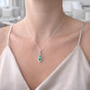 A close-up lifestyle shot of a woman wearing a silver pendant necklace with a marquise-cut green gemstone, paired with a light beige satin top.