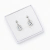 A pair of silver drop earrings with rectangular clear gemstones, presented in a white jewelry box on a white background.