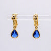 A pair of gold drop earrings with teardrop-shaped blue gemstones, displayed on a clear acrylic stand against a light gray background.