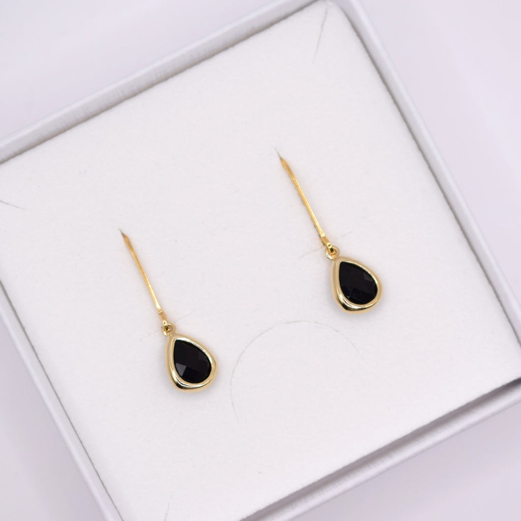 A pair of gold teardrop dangle earrings with black centers, presented in a white jewelry box.