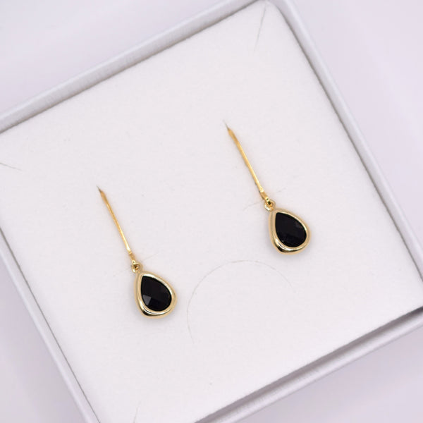 A pair of gold teardrop dangle earrings with black centers, presented in a white jewelry box.