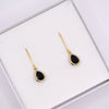 A pair of gold teardrop dangle earrings with black centers, presented in a white jewelry box.