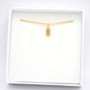 A delicate gold chain necklace with a small rectangular pendant containing clear stones, presented inside an open white jewelry box on a white background.