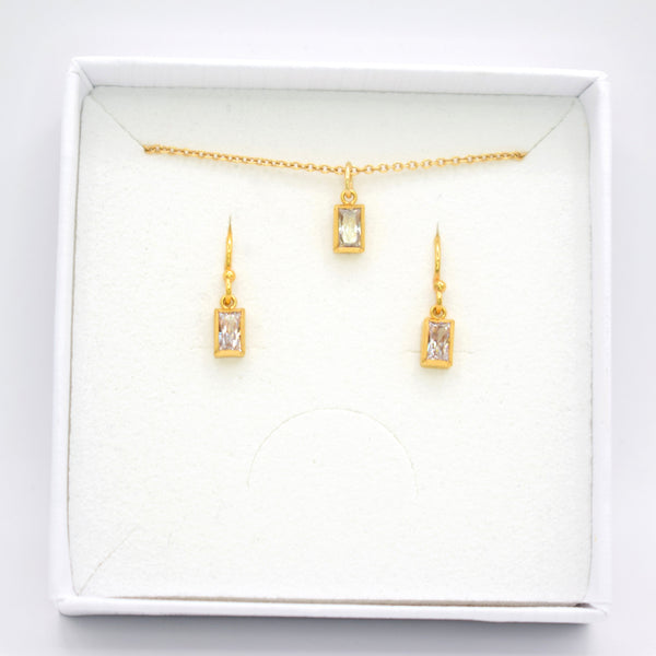 Gold jewelry set including a delicate chain necklace with a rectangular pendant and matching drop earrings, displayed inside a white square gift box on a white background.