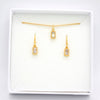 Gold jewelry set including a delicate chain necklace with a rectangular pendant and matching drop earrings, displayed inside a white square gift box on a white background.
