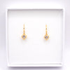 A pair of gold heart-shaped dangle earrings with clear gemstones, presented inside a white square jewelry box on a white background.