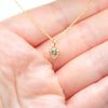 A delicate gold chain necklace with a small heart-shaped pendant held in a person's hand. The pendant features a clear, sparkling heart gemstone set in a gold bezel.