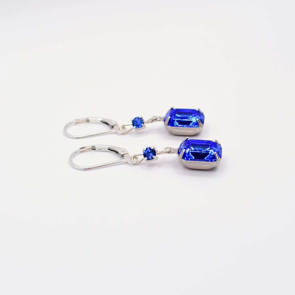A pair of silver leverback earrings featuring rectangular blue gemstones and small round blue accent stones, displayed on a clean white background.