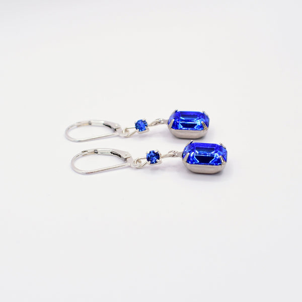 A pair of silver leverback earrings featuring rectangular blue gemstones and small round blue accent stones, displayed on a clean white background.