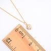 A gold chain necklace with a small heart-shaped pendant set with clear stones, shown next to a wooden ruler on a white background.