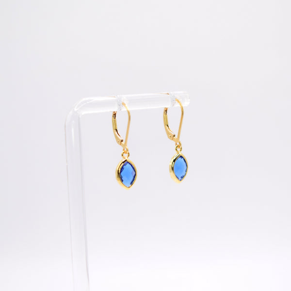 A pair of gold hoop earrings with marquise-cut blue gemstones, displayed on a clear acrylic stand against a white background.