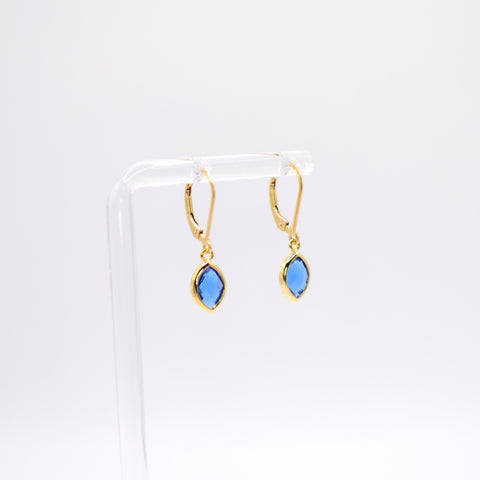 A pair of gold hoop earrings with marquise-cut blue gemstones, displayed on a clear acrylic stand against a white background.