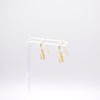 A pair of gold dangle earrings with small clear rectangular stones, displayed on a clear acrylic stand against a white background.
